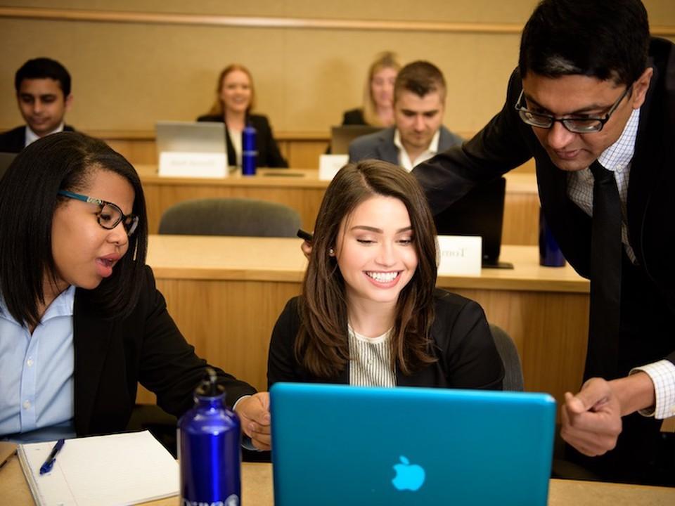 A lecture hall full of students working on laptops with a faculty member assisting 